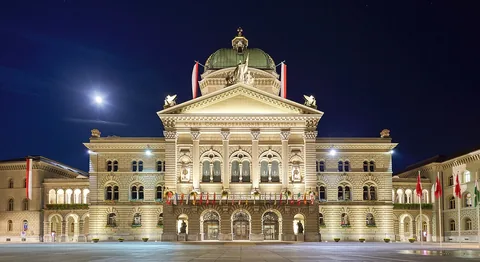 Federal Palace of Switzerland with full flags due to Indian President's state visit. Plaza view during full moon with clear night sky.